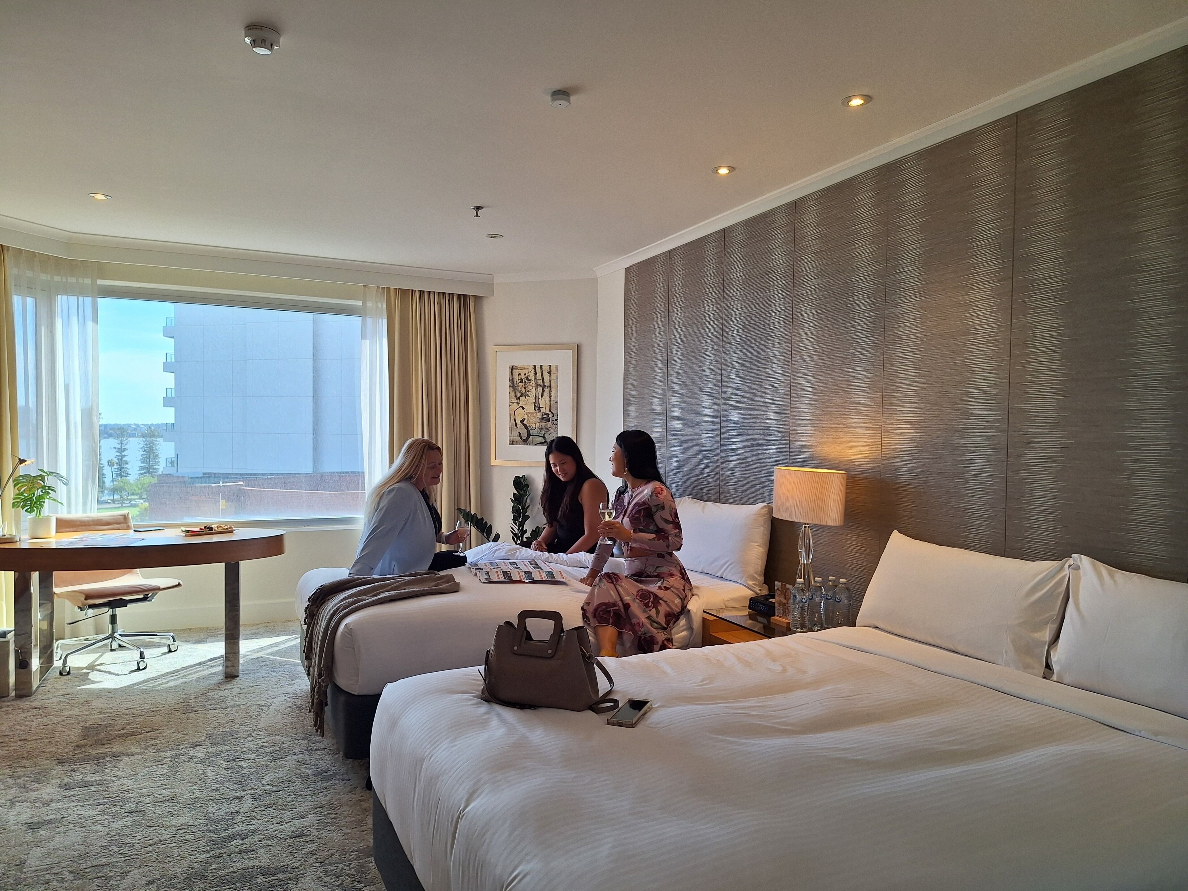 Une chambre d’hôtel avec un grand lit, un bureau avec une chaise, une fenêtre avec des rideaux et une vue sur les bâtiments environnants.