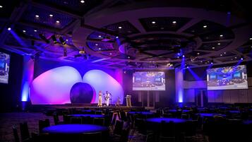 Un salón de conferencias con escenario, sillas y una pantalla grande.