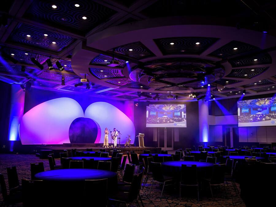 Un salón de conferencias con escenario, sillas y una pantalla grande.