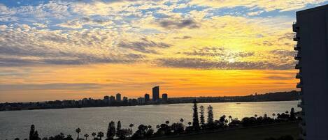 A sunset view from a high-rise building overlooking a city skyline and a body of water.