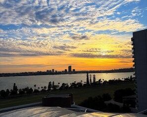 Une vue sur le coucher de soleil depuis un immeuble de grande hauteur, donnant sur les toits d’une ville et un plan d’eau.