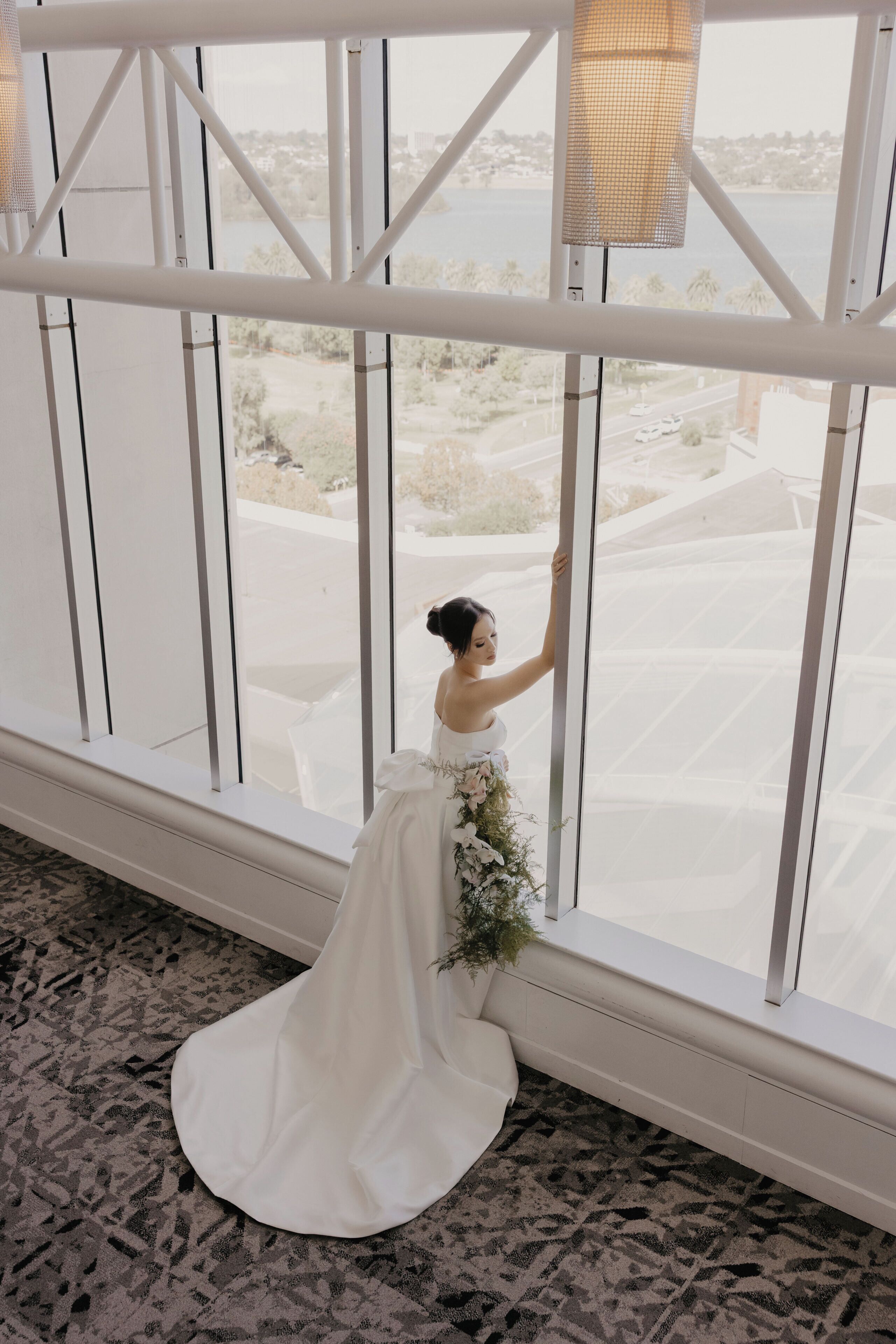 A person in a white dress standing by a large window with a view of a cityscape.