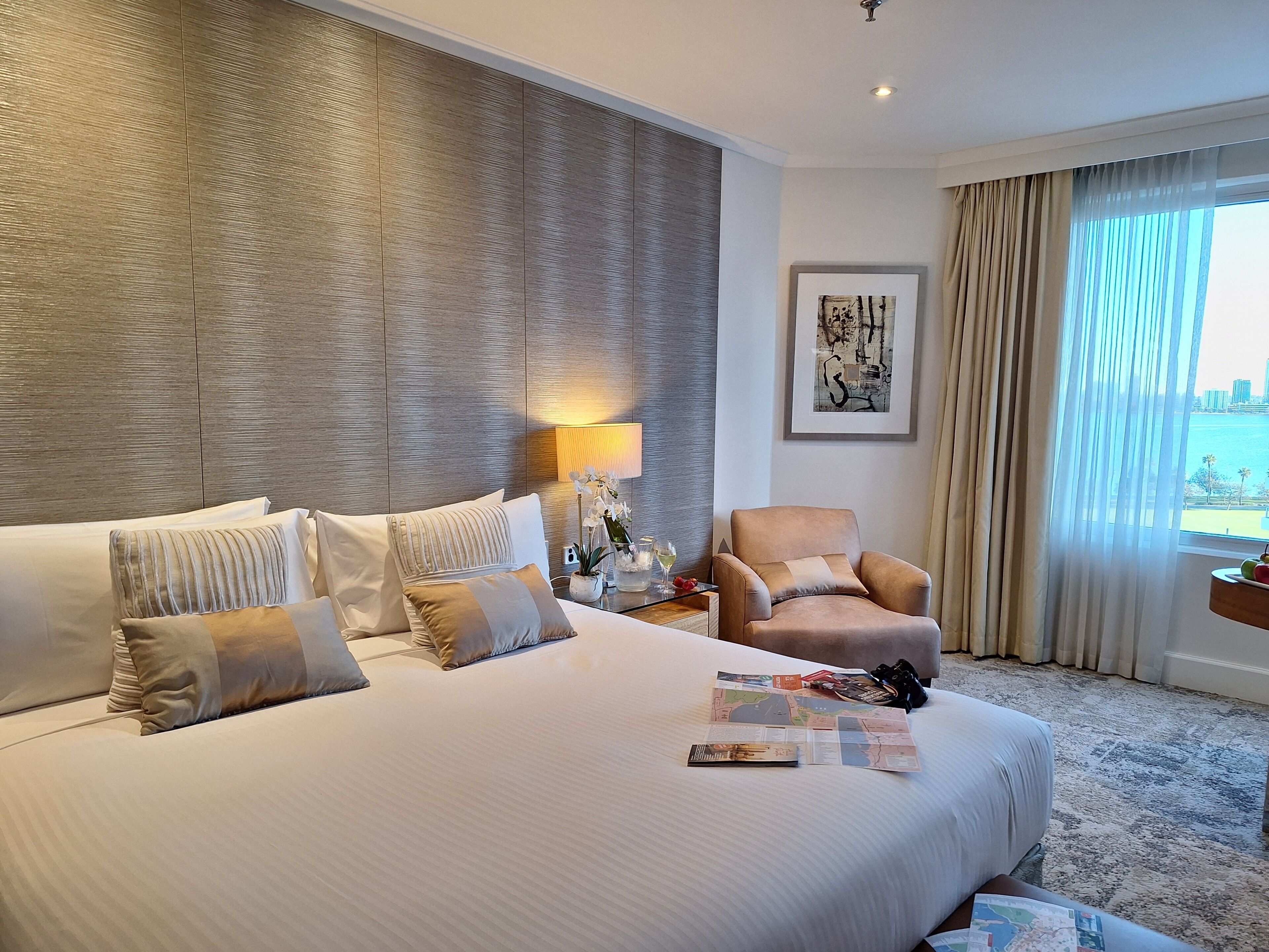 Habitación de hotel con una cama grande, una silla, una lámpara, una obra de arte enmarcada y vista al mar.