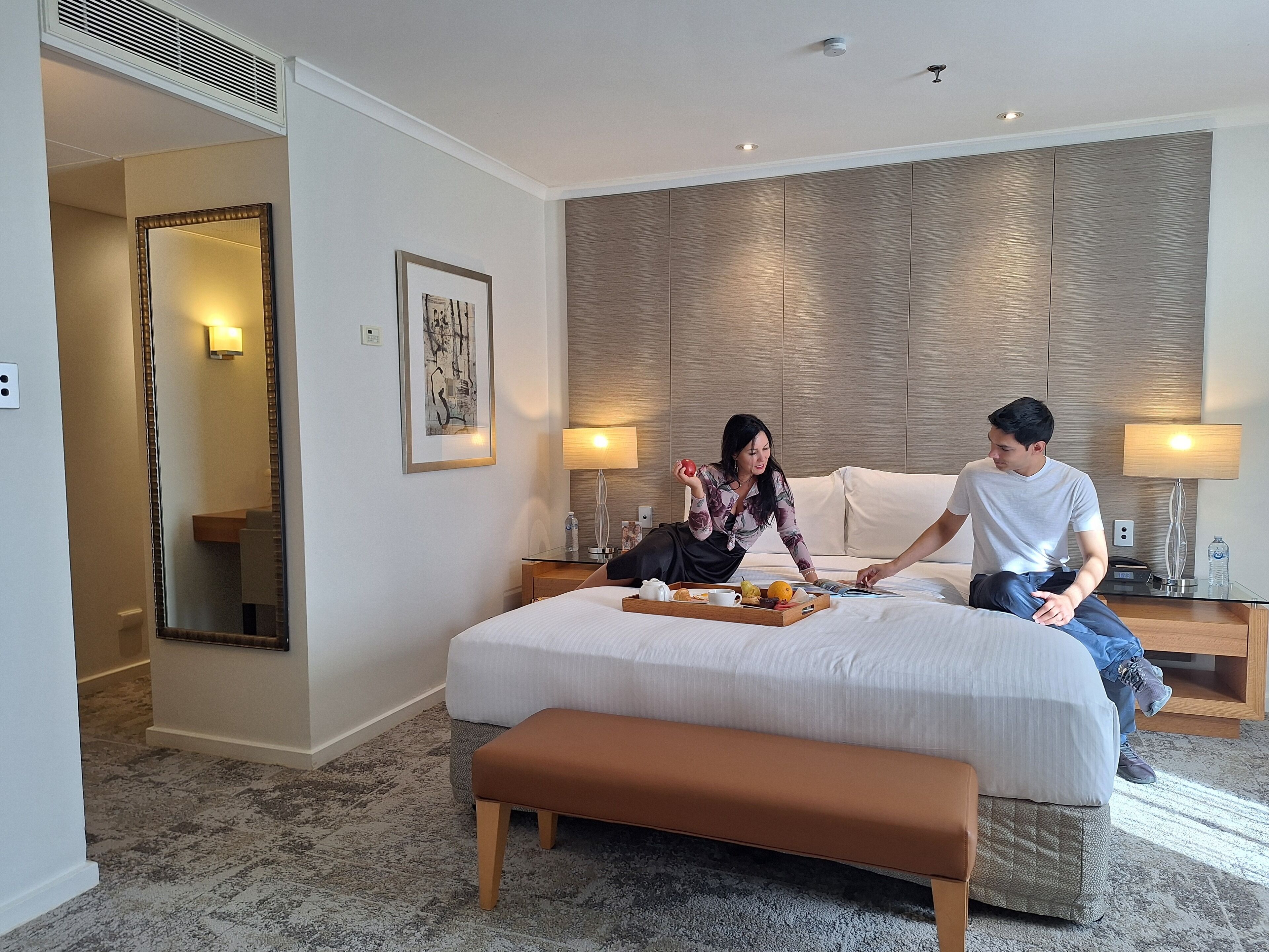 A hotel room with a large bed, bedside tables with lamps, a mirror, and a framed picture on the wall.