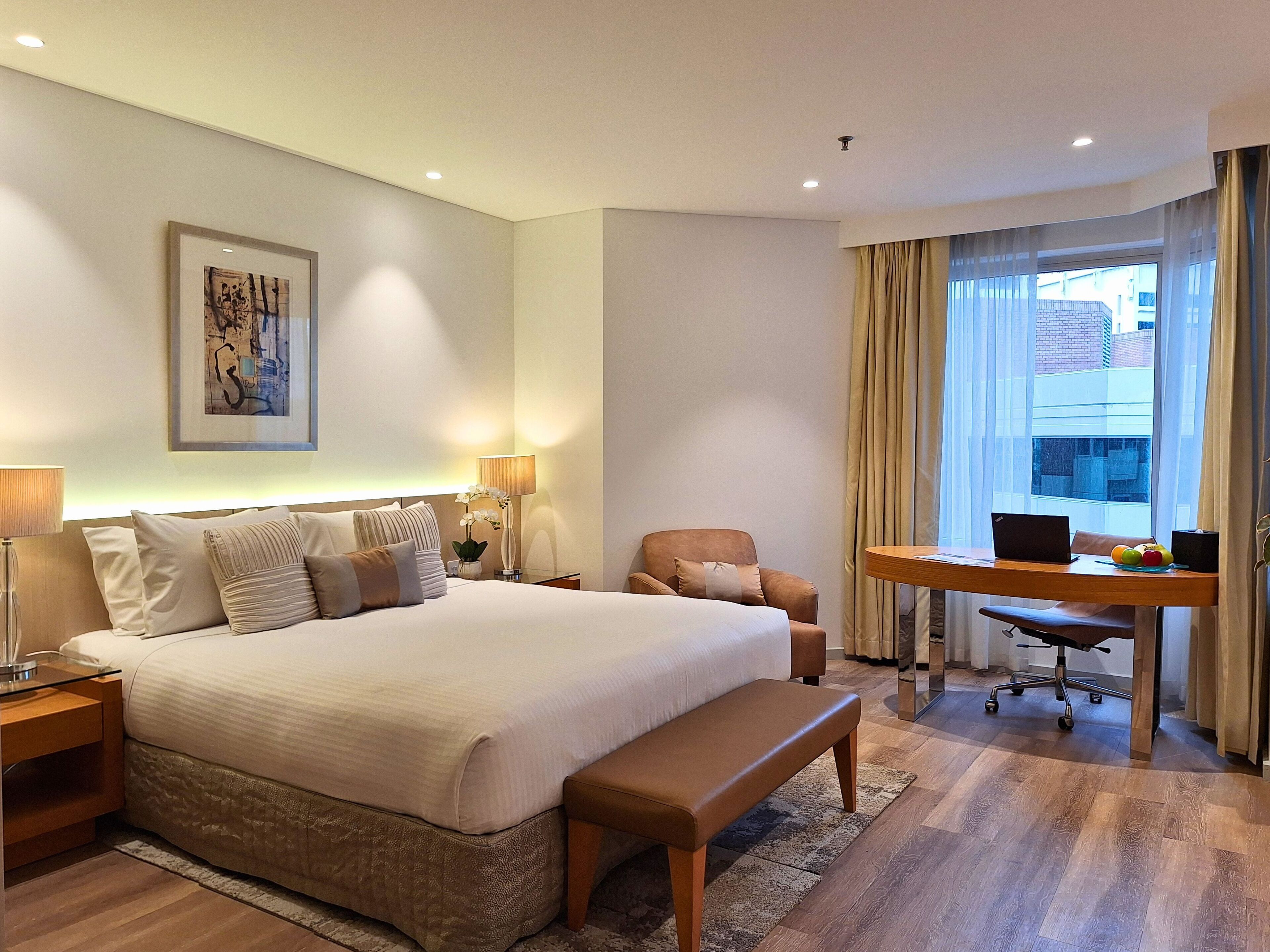 Una habitación de hotel con una cama grande, un escritorio con una computadora portátil, una silla y una ventana con cortinas.