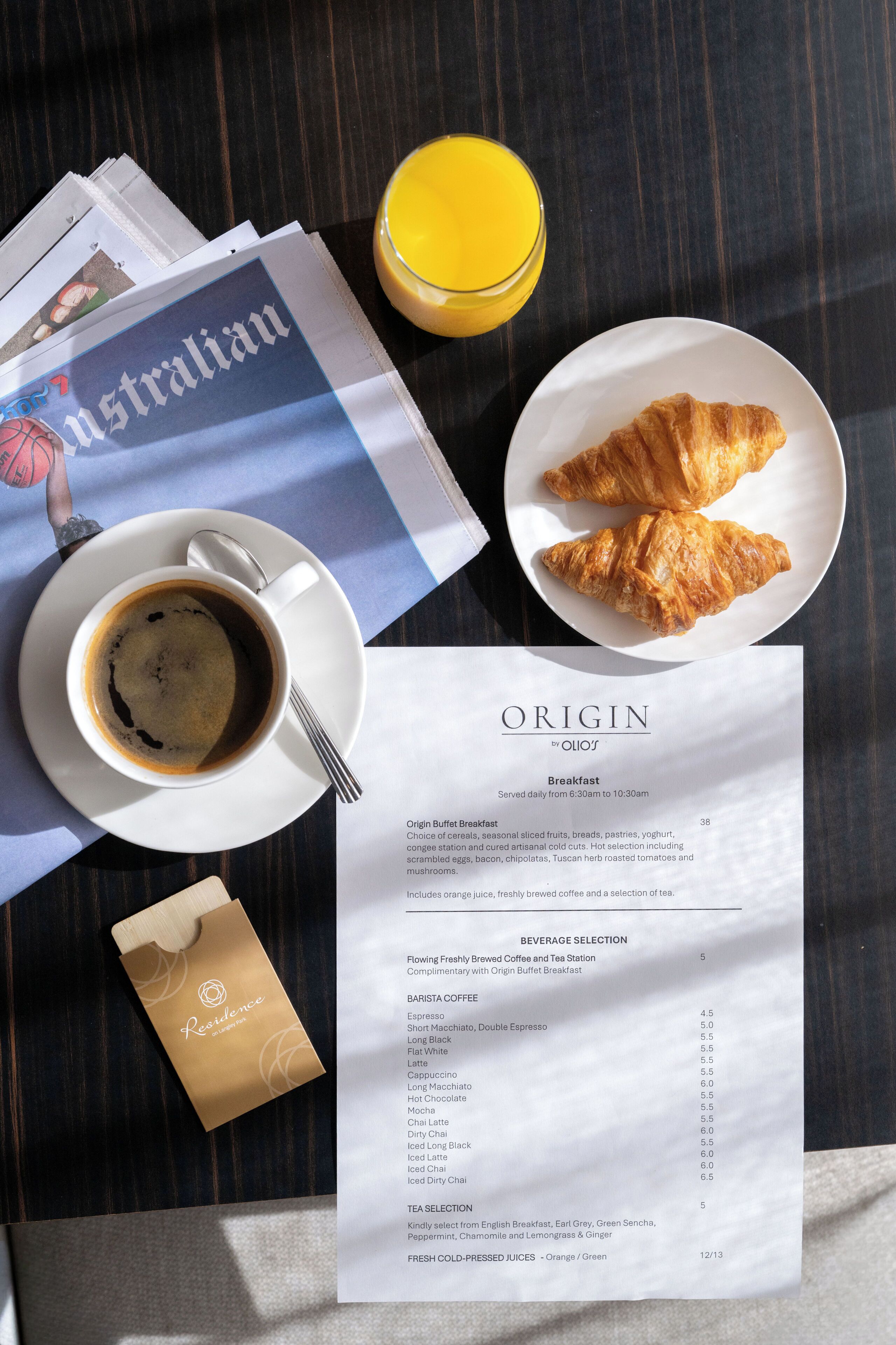 A breakfast setting with a menu, a croissant, a glass of orange juice, and a cup of coffee on a wooden table.