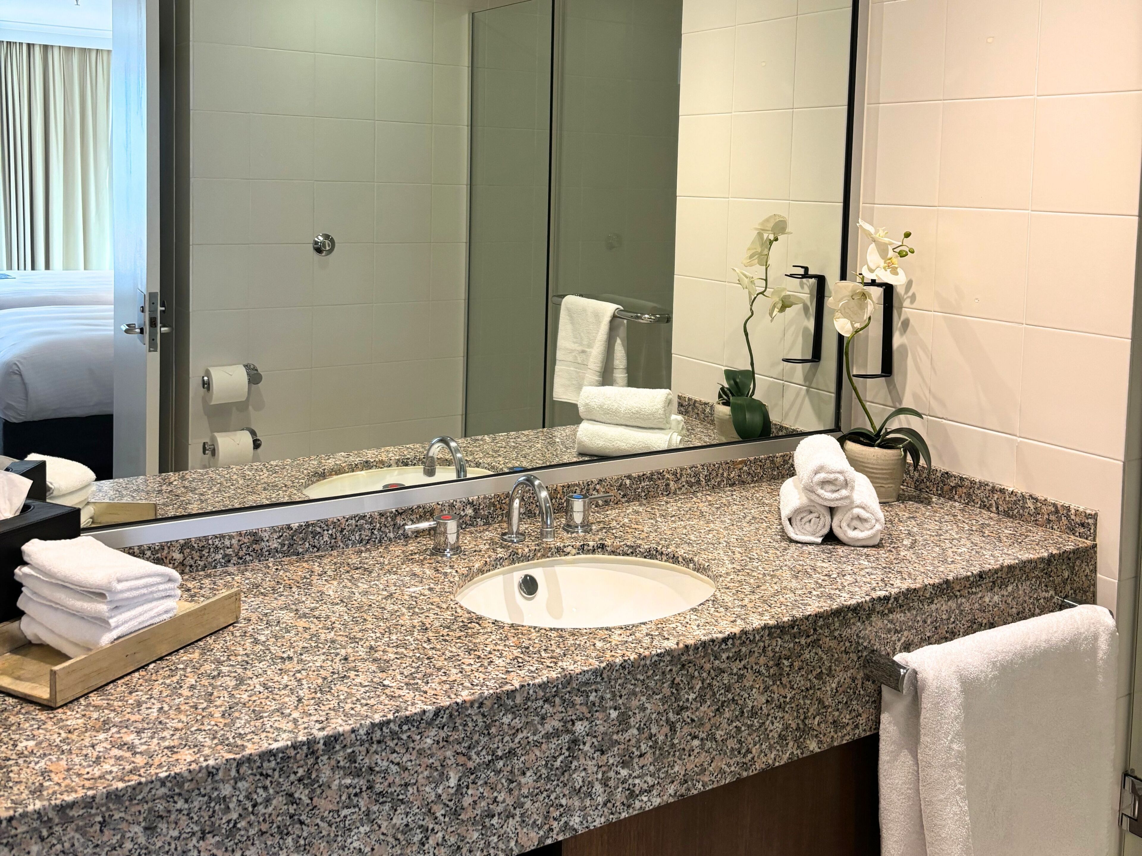 Une salle de bain d’hôtel avec un lavabo doté d’un plan en granit, un grand miroir et une orchidée en pot.