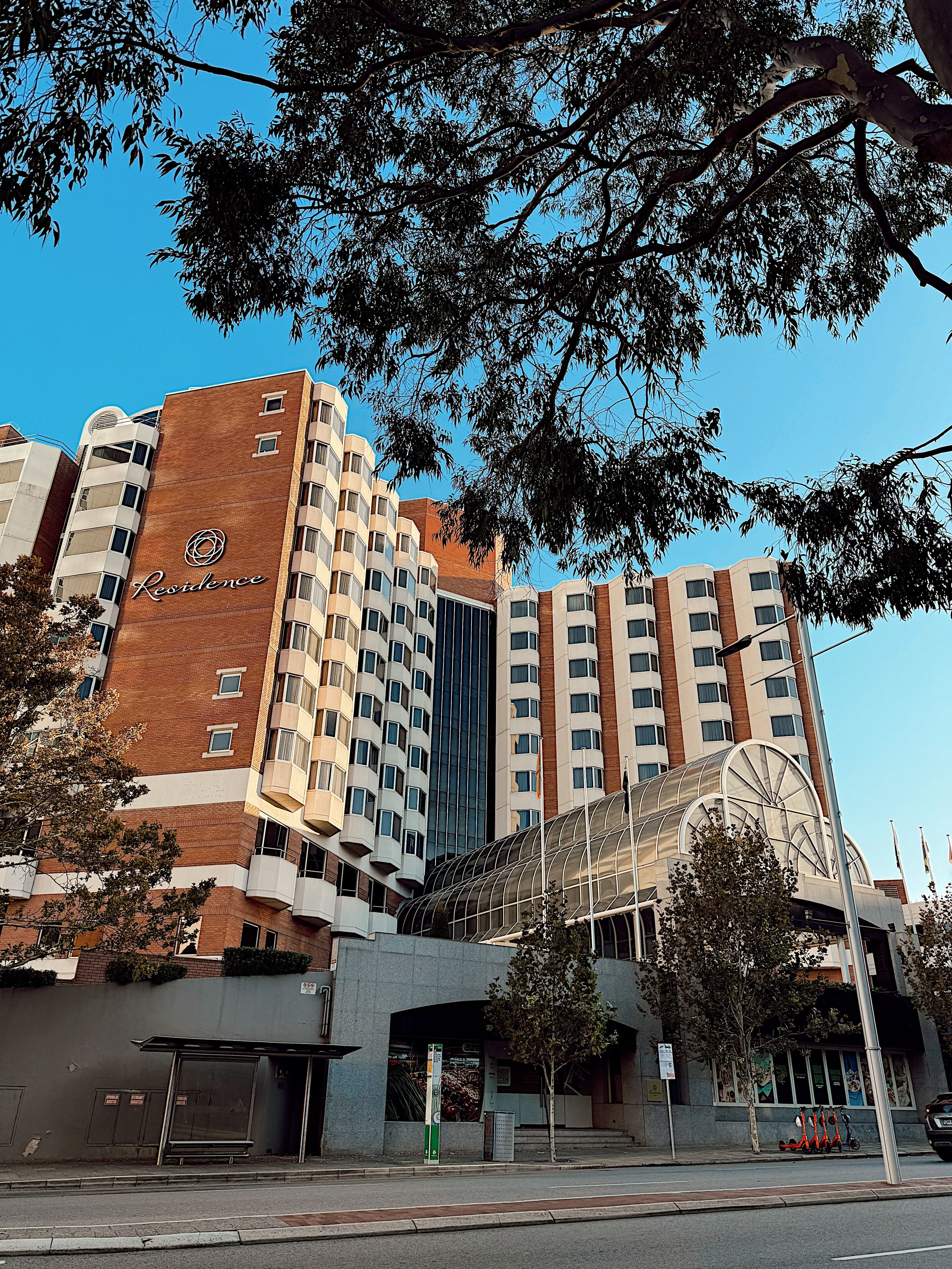 A multi-story hotel with a prominent 'Residence' sign, a covered entrance, and a parking area with scooters.