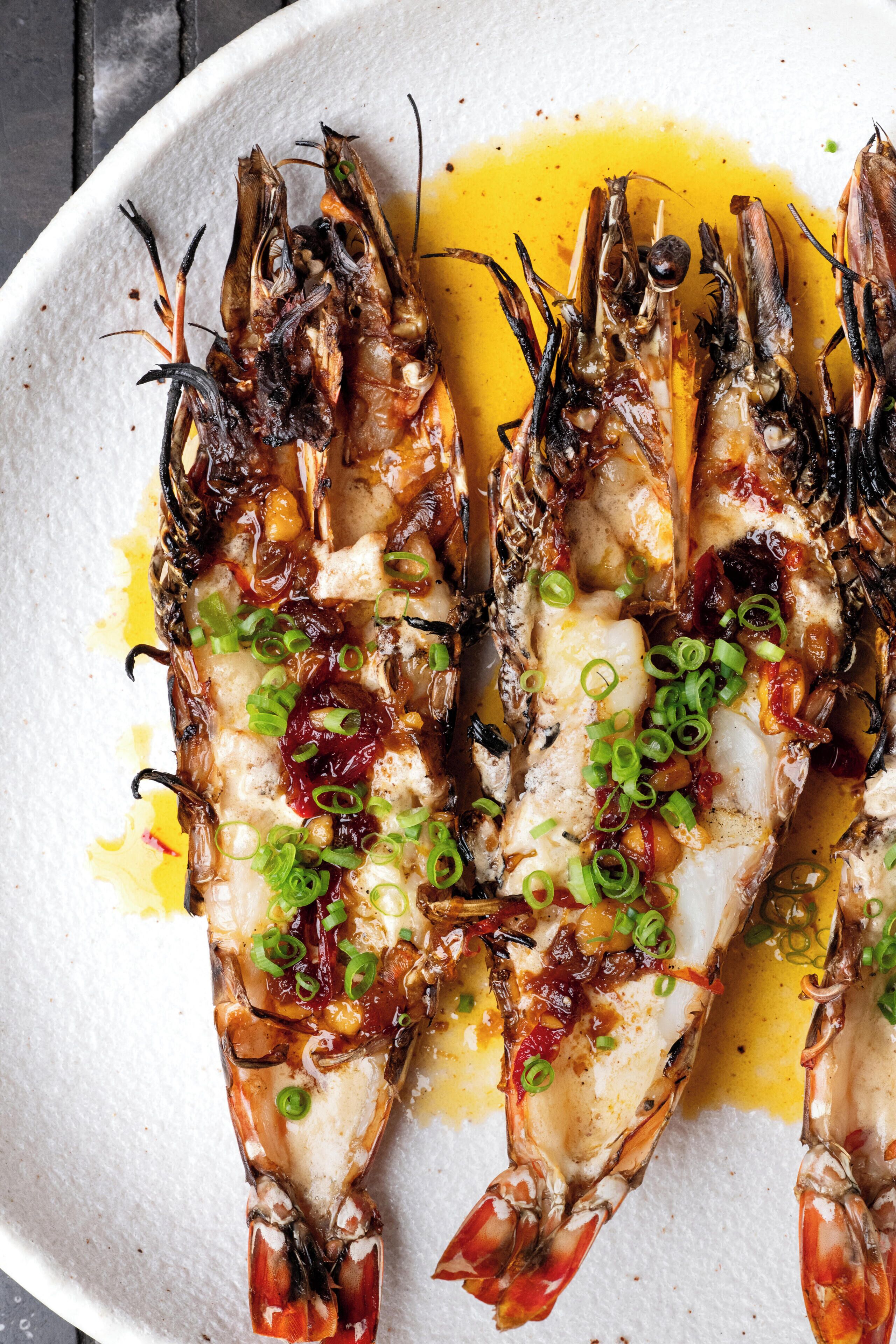 Two grilled lobsters on a white plate with green onions and a yellow sauce.