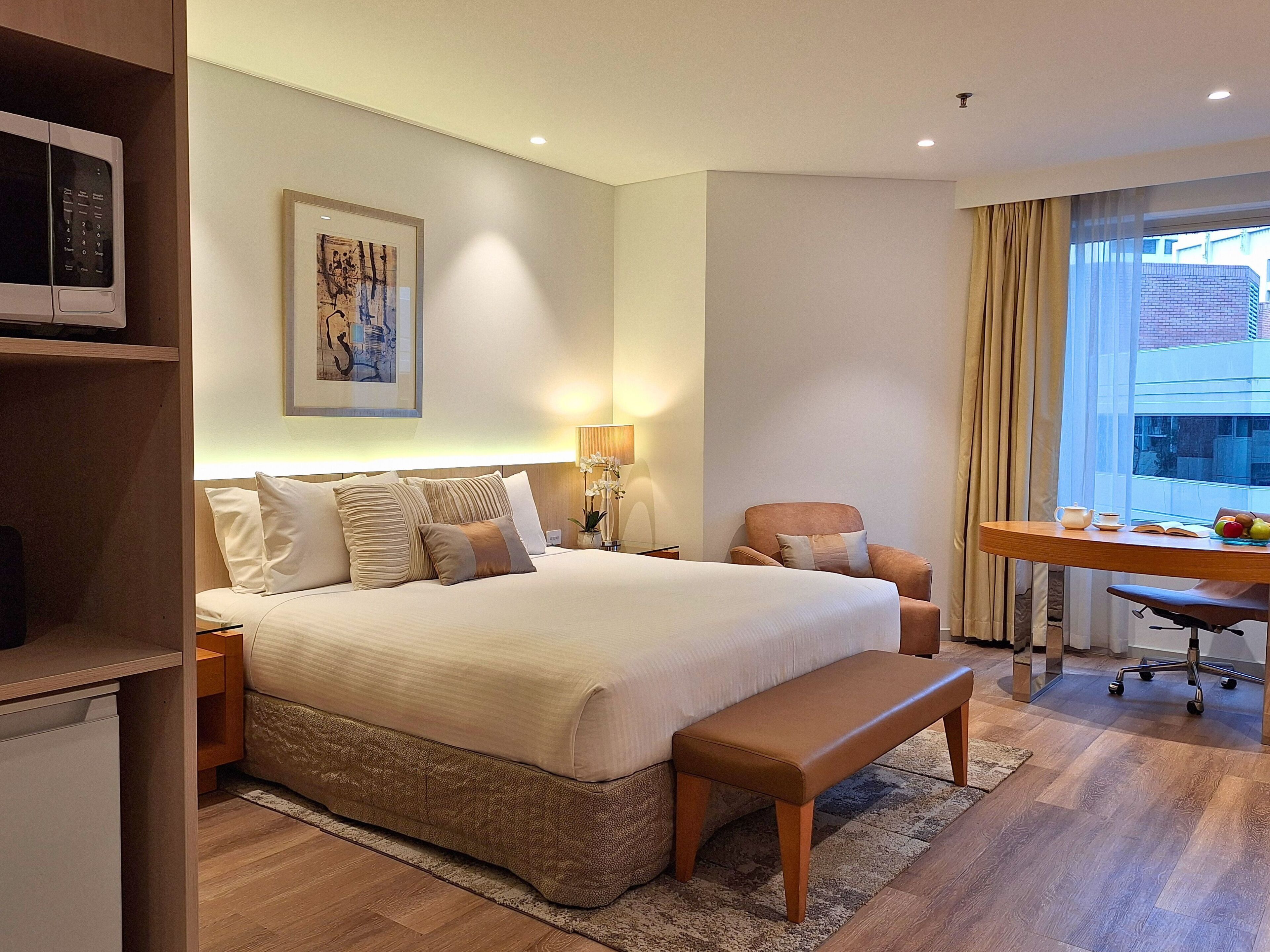 A hotel room with a large bed, bedside tables, a desk with a chair, a microwave, and a window with curtains.