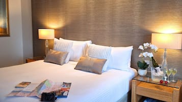 Ein ordentlich gemachtes Bett mit Kissen, einer Karte und einer Kamera darauf. Es gibt zwei Nachttische mit Lampen und einen Blumenstrauß in einer Vase.