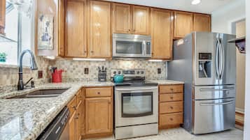 A kitchen with wooden cabinets, stainless steel appliances, a granite countertop, and a tiled backsplash.