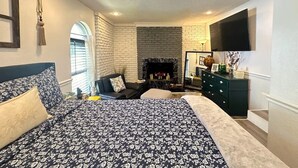 Un dormitorio con una cama grande, una chimenea, un televisor montado en la pared y un escritorio con una silla.