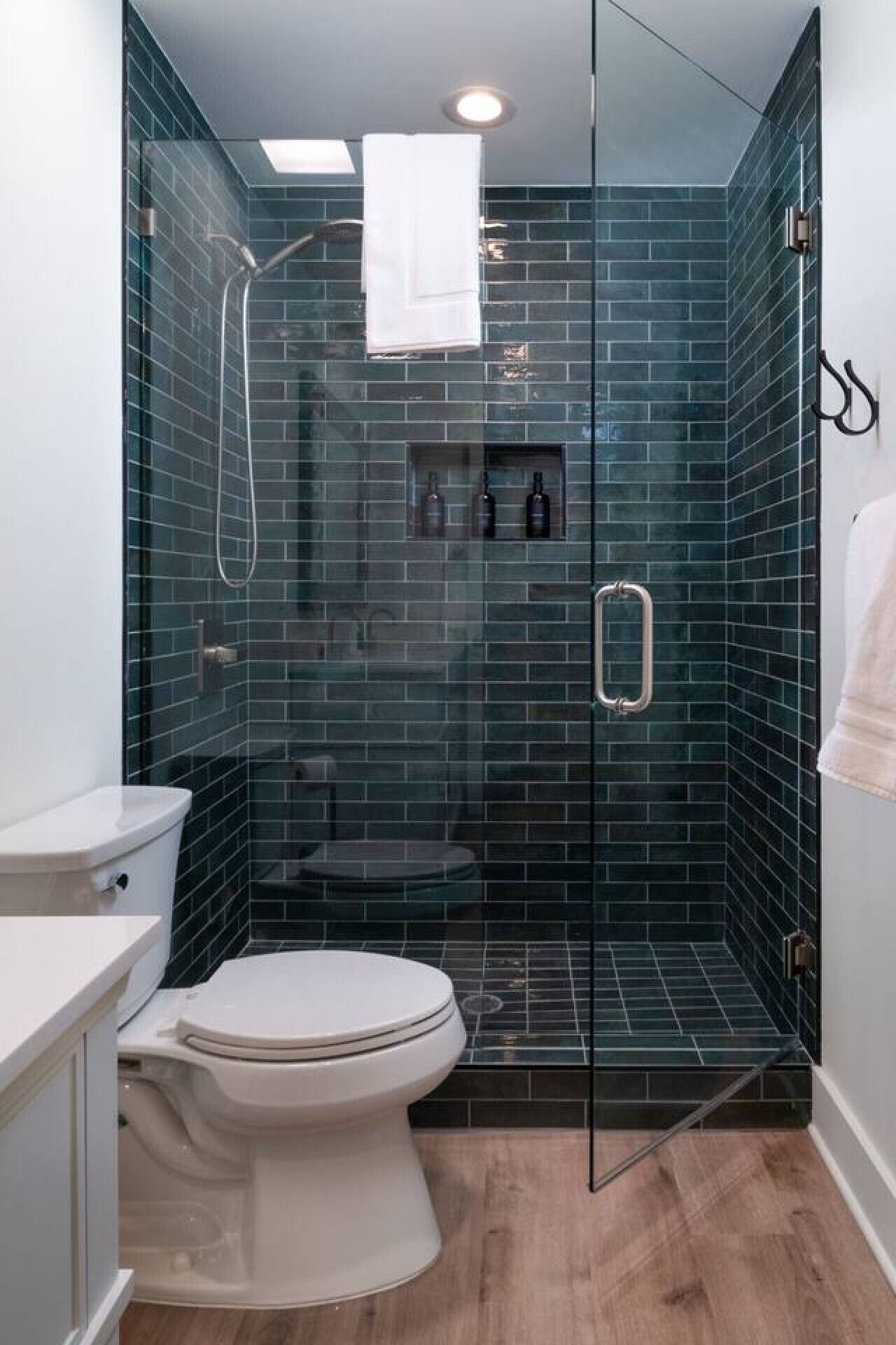 Ein Badezimmer mit Duschkabine aus Glas, einer weißen Toilette und einem Waschbecken mit weißer Arbeitsplatte.