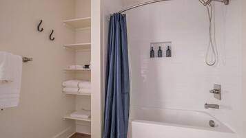 Une salle de bain avec une douche, un porte-serviettes et une étagère où sont pliés les serviettes.