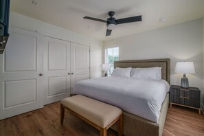 A bedroom with a bed, a bench, a nightstand, a lamp, a ceiling fan, and a window.