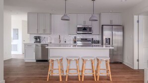 A modern kitchen with white cabinets, stainless steel appliances, and a central island with bar stools. - 5 Star Flat Downtown Trussville (Trussville)