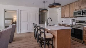 A modern kitchen with a central island, bar stools, wooden cabinets, stainless steel appliances, and pendant lighting. - Luxury Penthouse in Entertainment District (Trussville)
