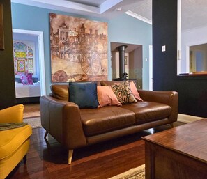 A living room with a brown leather sofa, a yellow armchair, and a large painting of a historical building.