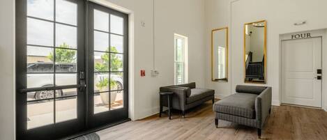 A hotel lobby with a large glass door, a sofa, a chair, a mirror, and a door labeled 'FOUR'.