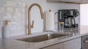 Eine moderne Küche mit einer Spüle aus Edelstahl, einem Wasserhahn in Goldoptik, einer Kaffeemaschine und einer Handseifenflasche.