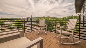 Ein Balkon mit zwei Schaukelstühlen, einer Holzterrasse und Blick auf einen Parkplatz sowie Grünflächen.