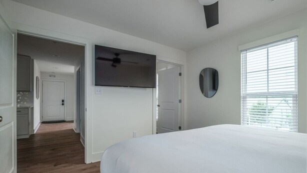 Ein Schlafzimmer mit einem großen Bett, einem Deckenventilator, einem an der Wand montierten Fernseher und einem Fenster mit Jalousien.