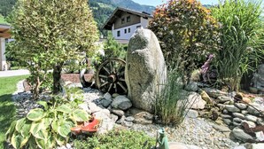 A garden with a large rock, a wooden wheel, and various plants. - Paradiso by Interhome (Ramsau im Zillertal)