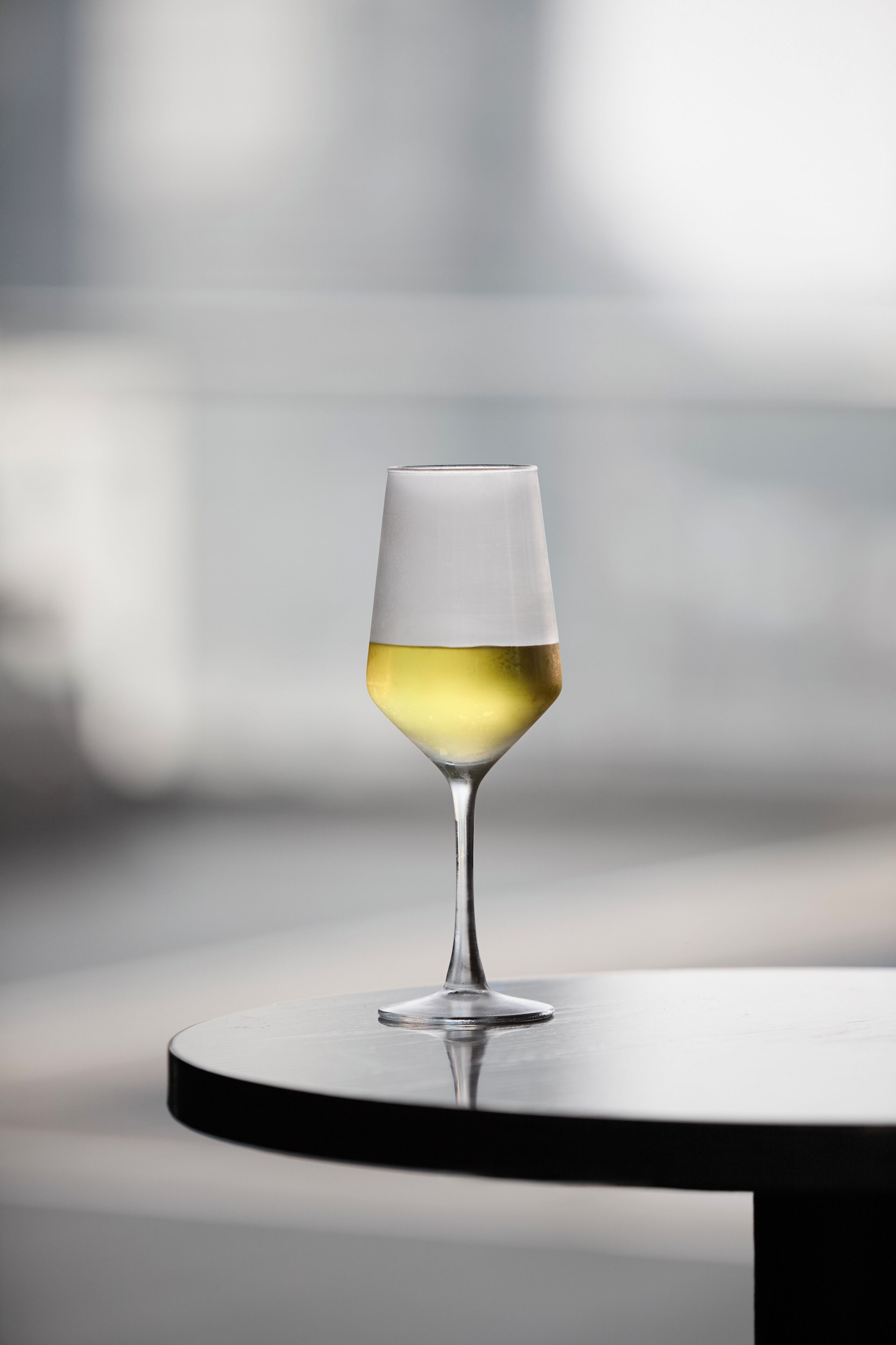 Een wijnglas met een witte vloeistof op een ronde tafel.