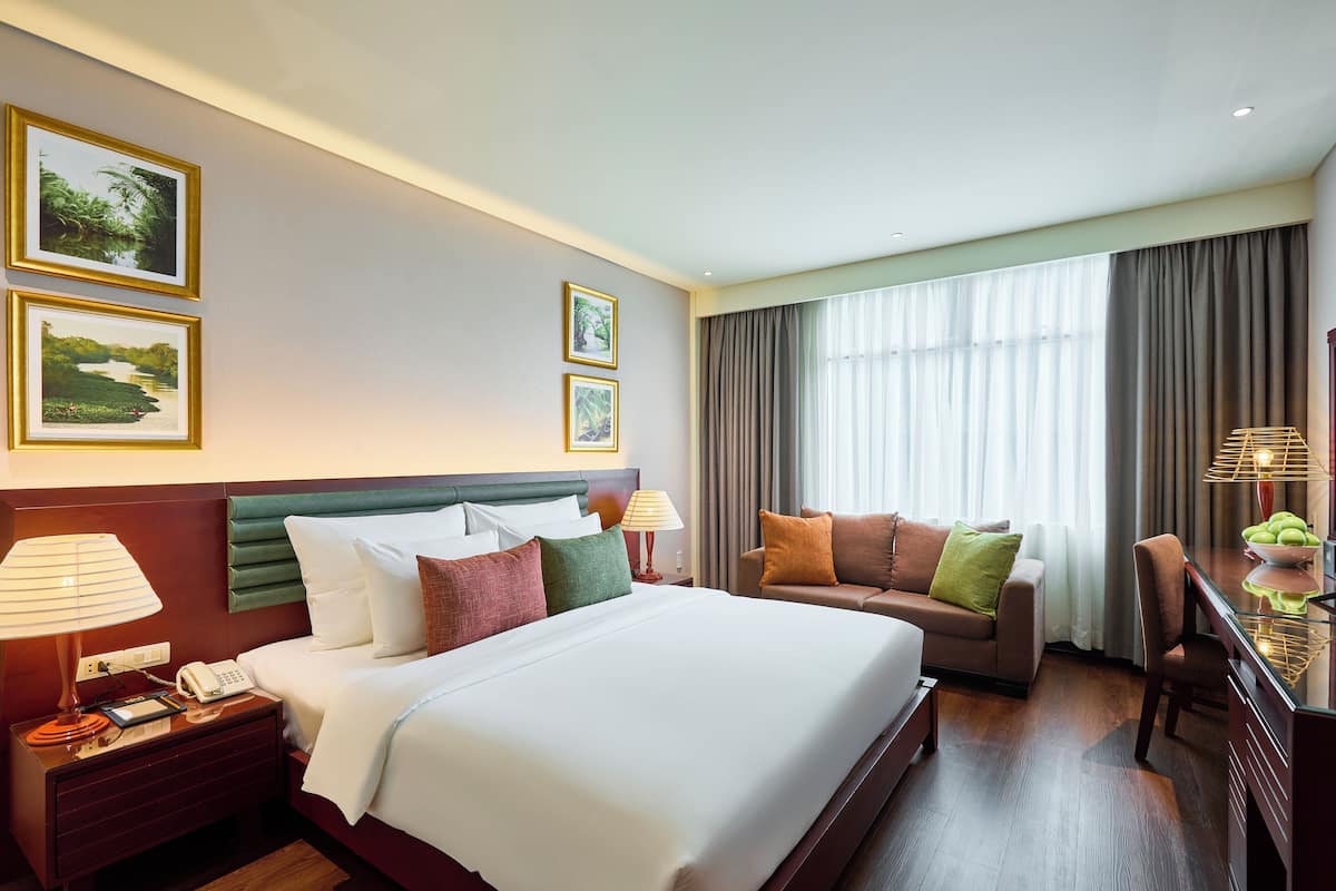 Ein Hotelzimmer mit einem großen Bett, einer Couch, einem Schreibtisch mit Lampe und zwei gerahmten Bildern an der Wand.
