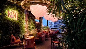 A modern lounge area with a wooden floor, comfortable seating, a neon sign, and a view of the cityscape. - Kin Hotel Thi Sach (Ho Chi Minh City)