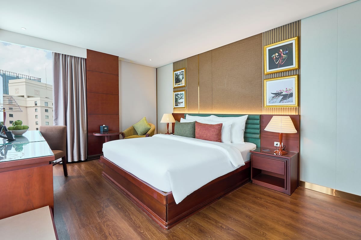 Ein Hotelzimmer mit einem großen Bett, einem Schreibtisch mit Stuhl, einem Nachttisch und Blick auf die Stadtlandschaft.