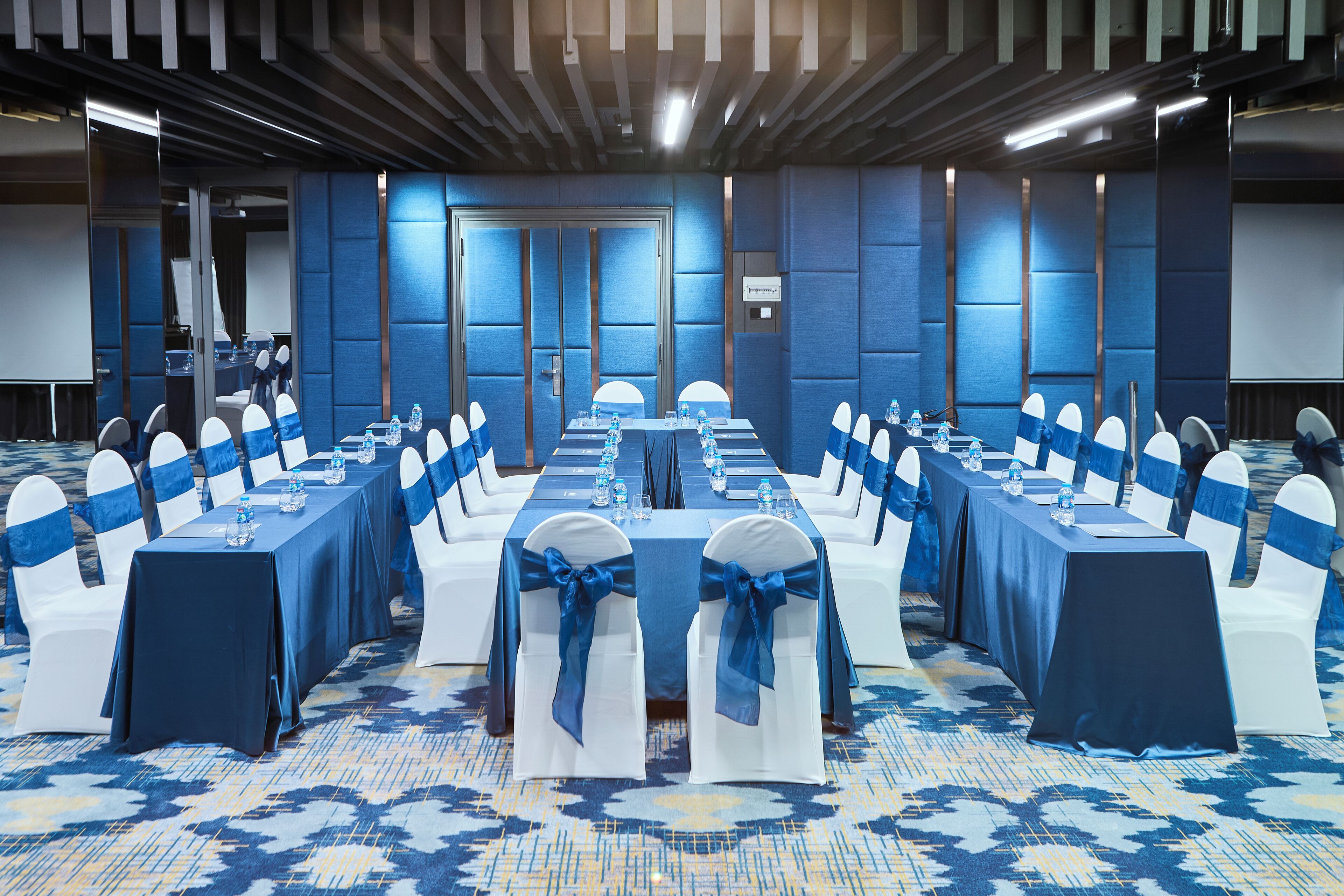 A conference room with rows of tables and chairs, equipped with water bottles and nameplates.