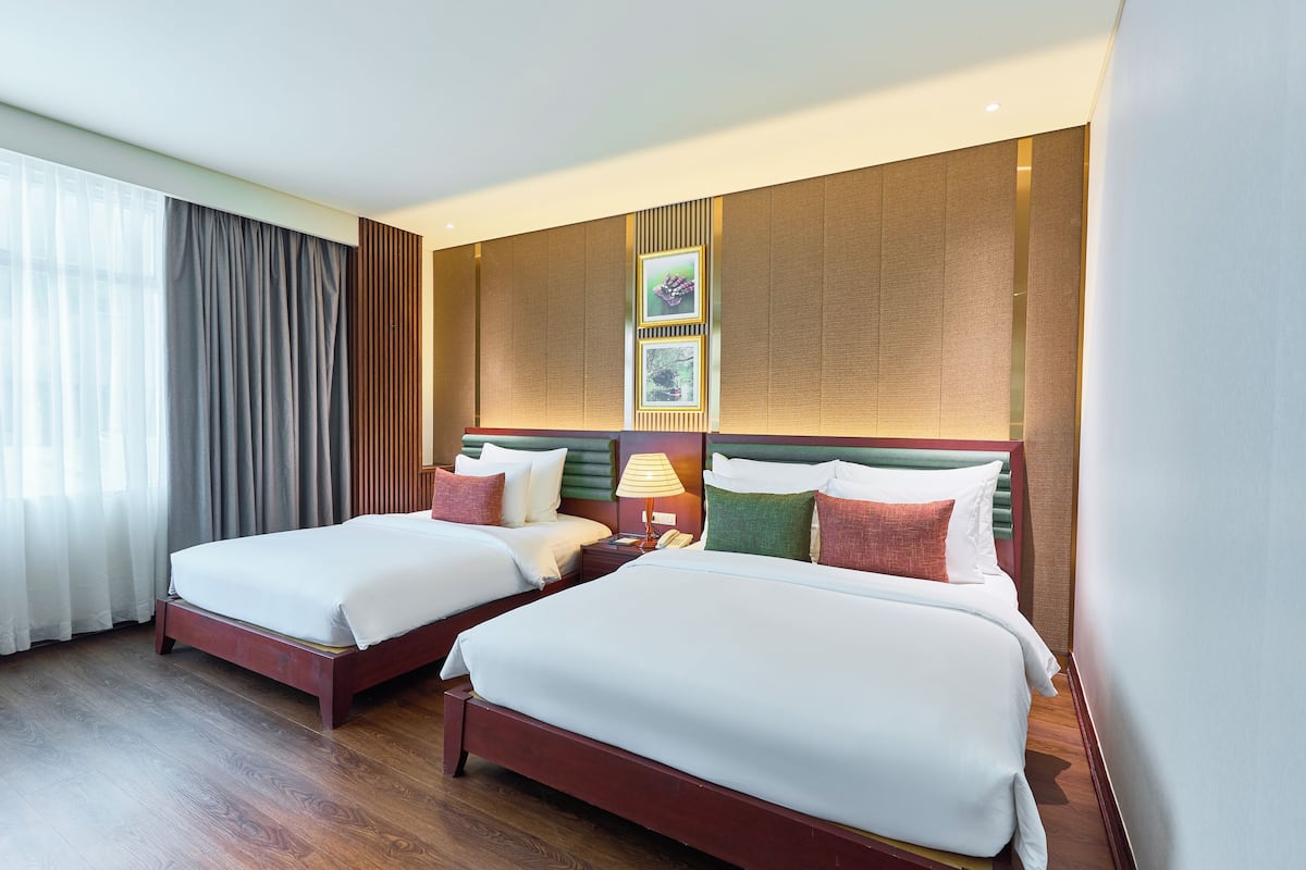 Ein Hotelzimmer mit zwei Betten, Holzboden, einem großen Fenster mit Vorhängen und einer Wand mit gerahmten Bildern.