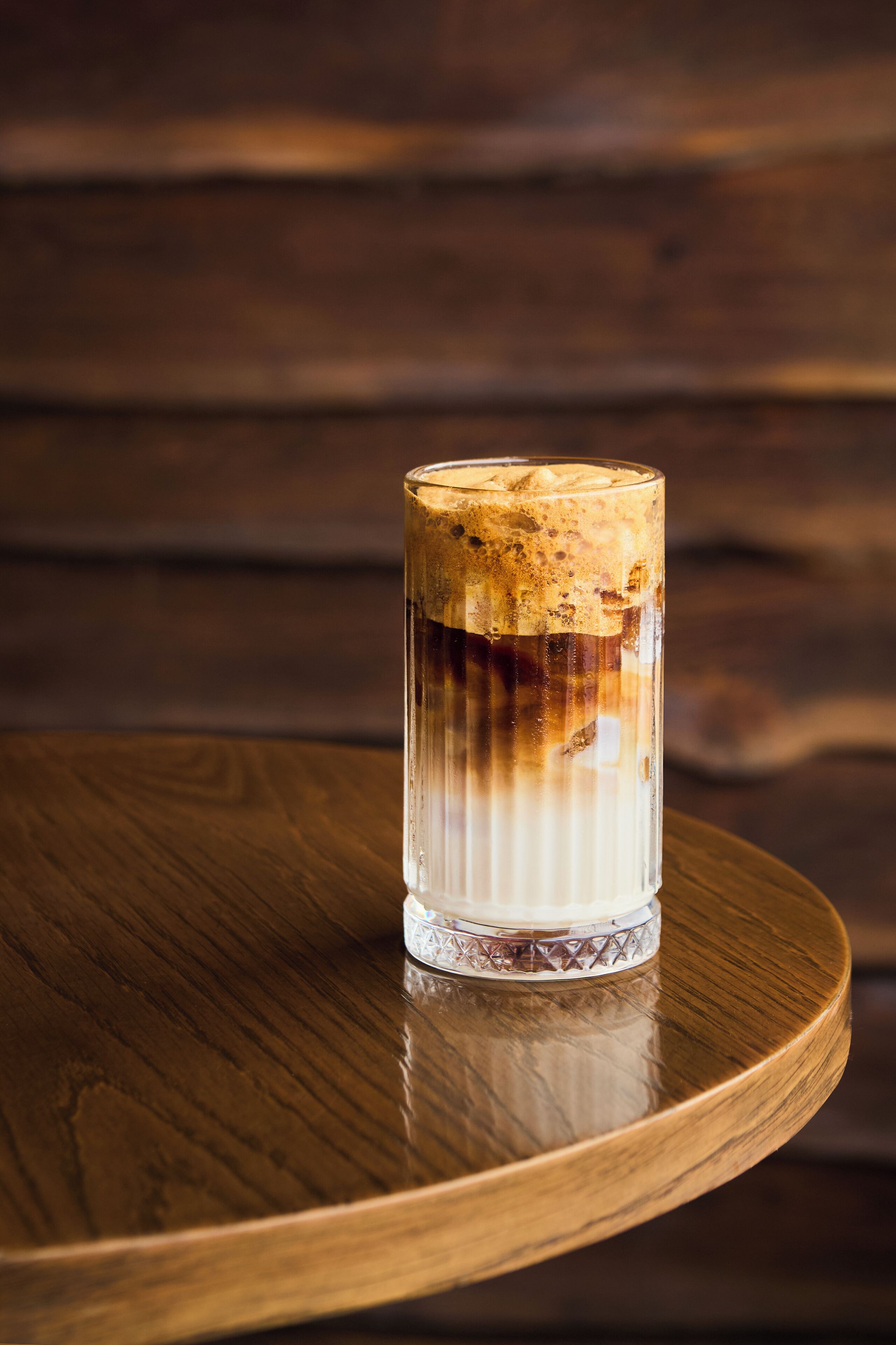 A glass of iced coffee on a wooden table with a wooden background.