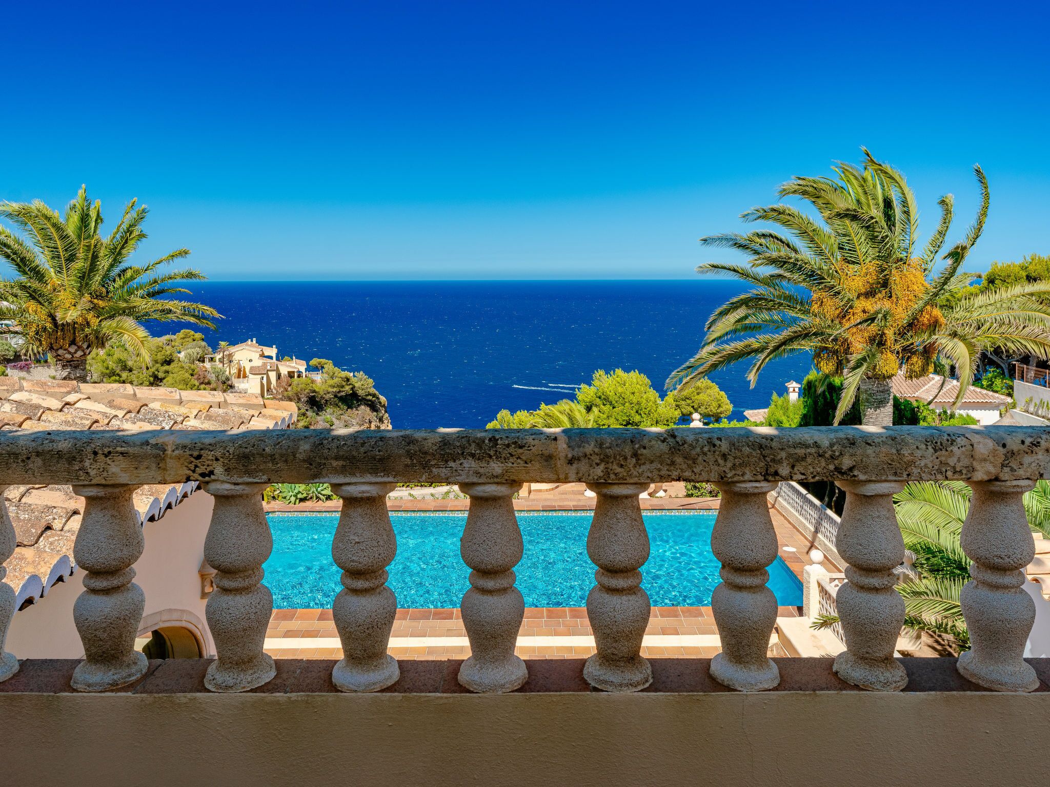 A stone balustrade overlooking a clear blue sea with a pool in the foreground.