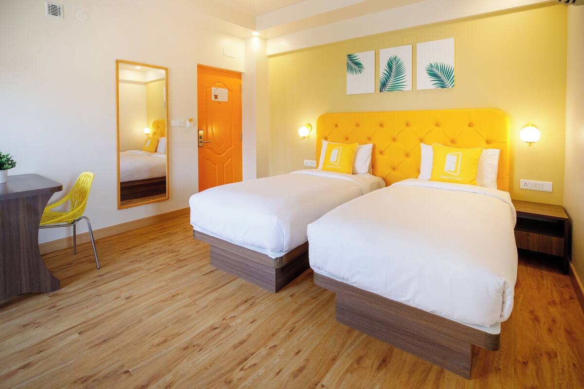 Une chambre d’hôtel avec deux lits, un plancher en bois, un bureau, une chaise et un miroir.