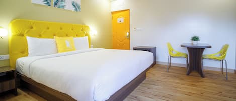 Habitación de hotel con una cama grande, una mesita de noche, una pequeña mesa con sillas y una puerta.