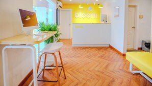 A reception area with a wooden herringbone floor, a desk with a computer, a chair, and a yellow bench. - Bloom Hotel - HAL Old Airport Rd (Bengaluru)