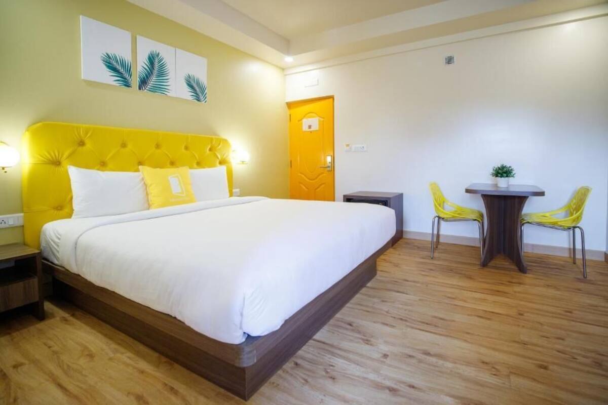 Une chambre d’hôtel avec un grand lit, une tête de lit en bois, une petite table avec des chaises et une porte.
