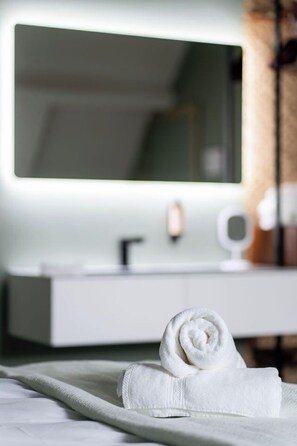 A neatly made bed with a rolled white towel and a white bedside table with a mirror.