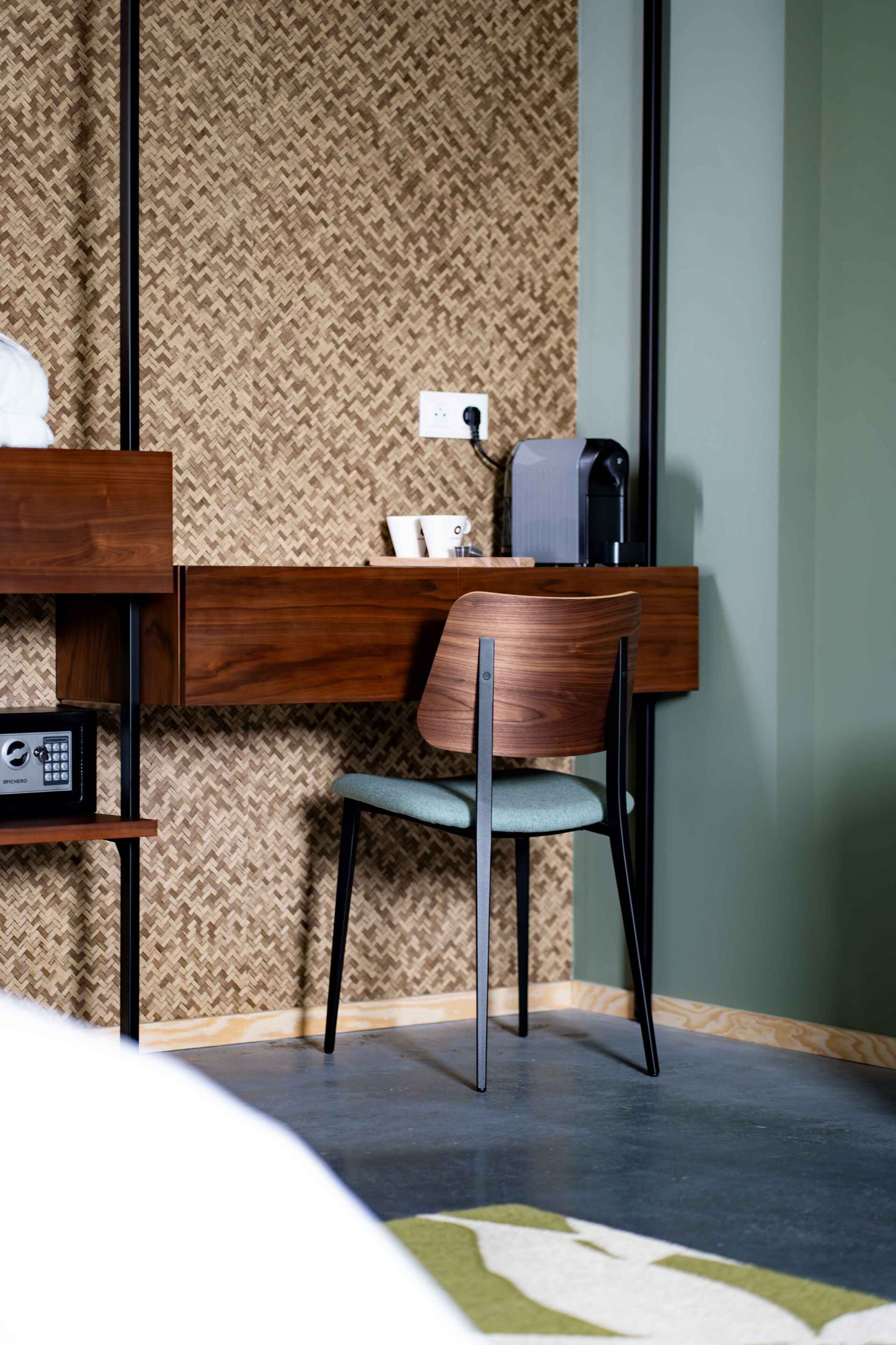 A hotel room with a wooden desk, a chair, a coffee maker, and a small shelf with a radio.