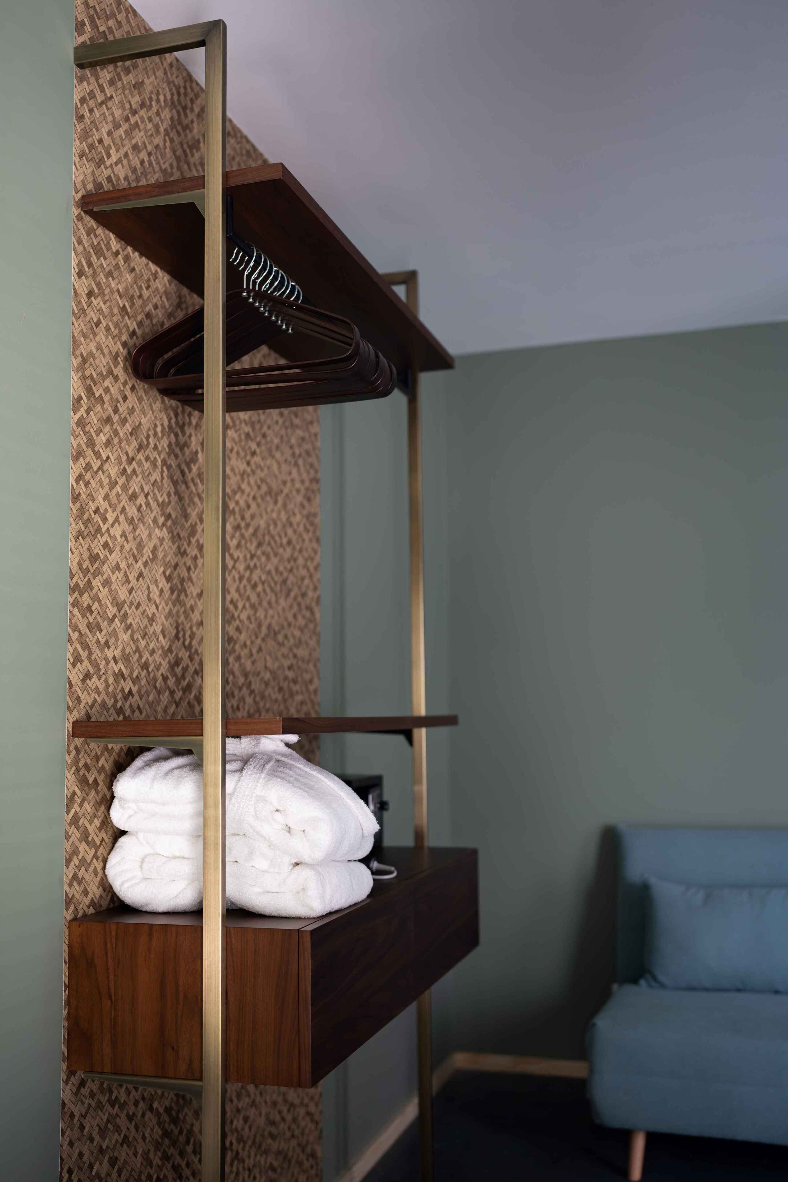 A room with a wooden shelf unit against a textured wall, holding folded towels and a hanging garment.