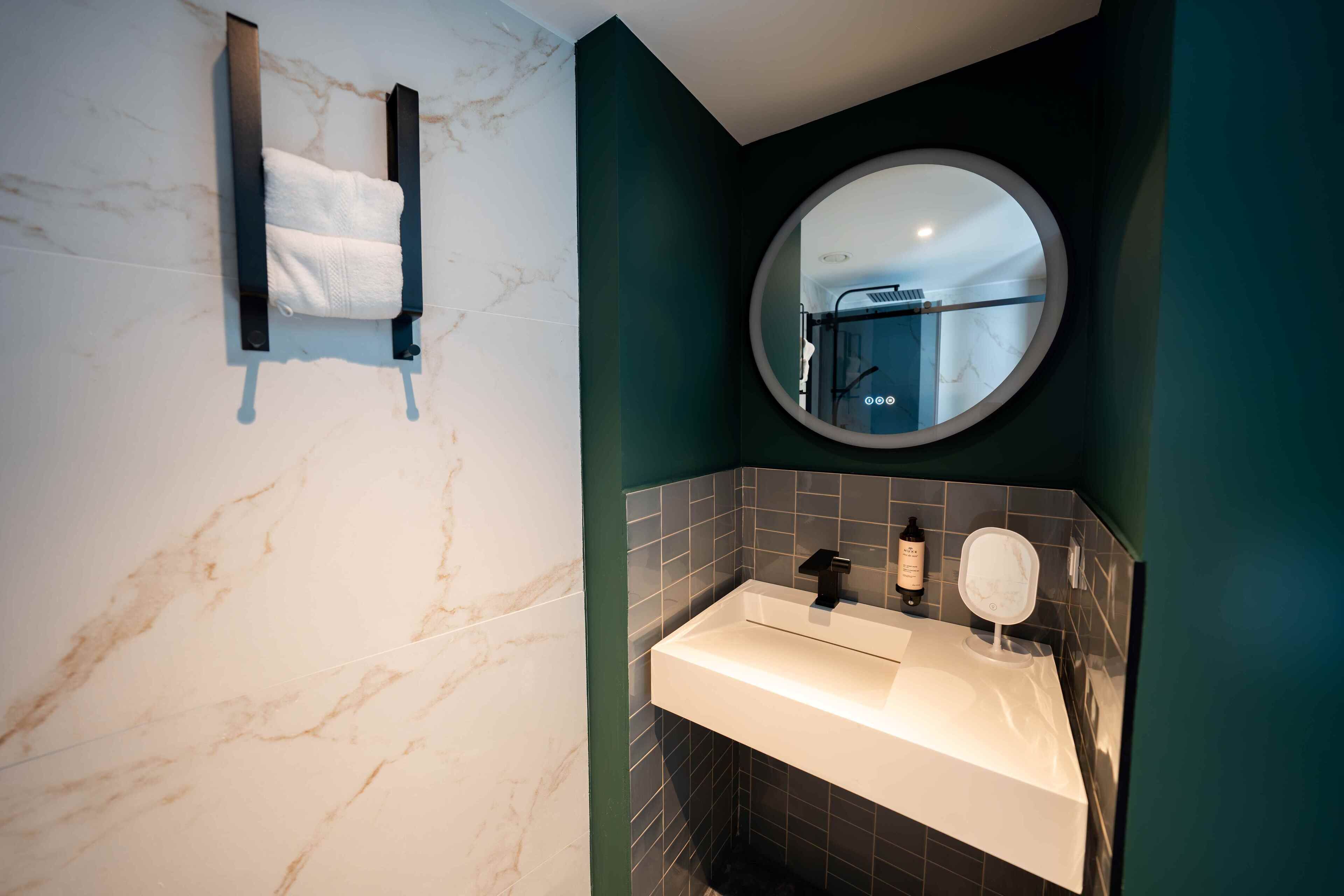 Une salle de bain avec un mur en marbre, un porte-serviettes, un lavabo avec un miroir et un miroir rond au-dessus du lavabo.