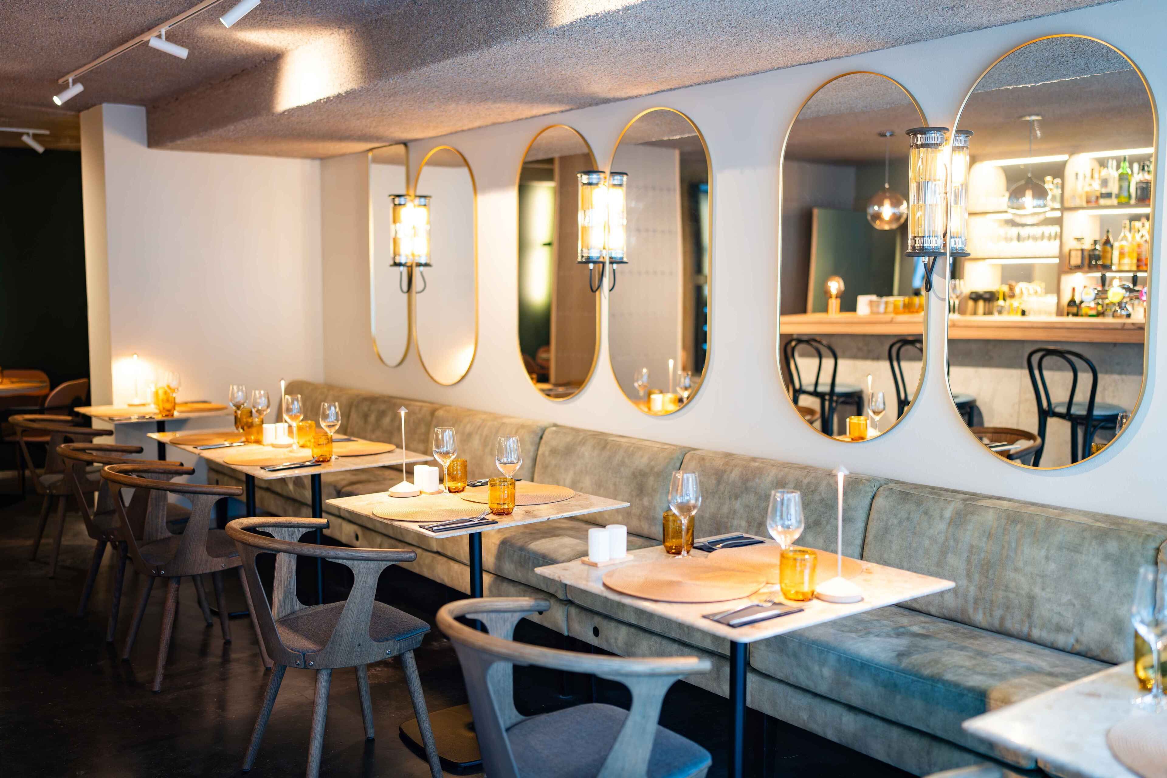 Ein Restaurantinnenraum mit ovalen Spiegeln, Holzsesseln und Tischen, gedeckt mit Gläsern und Flaschen.