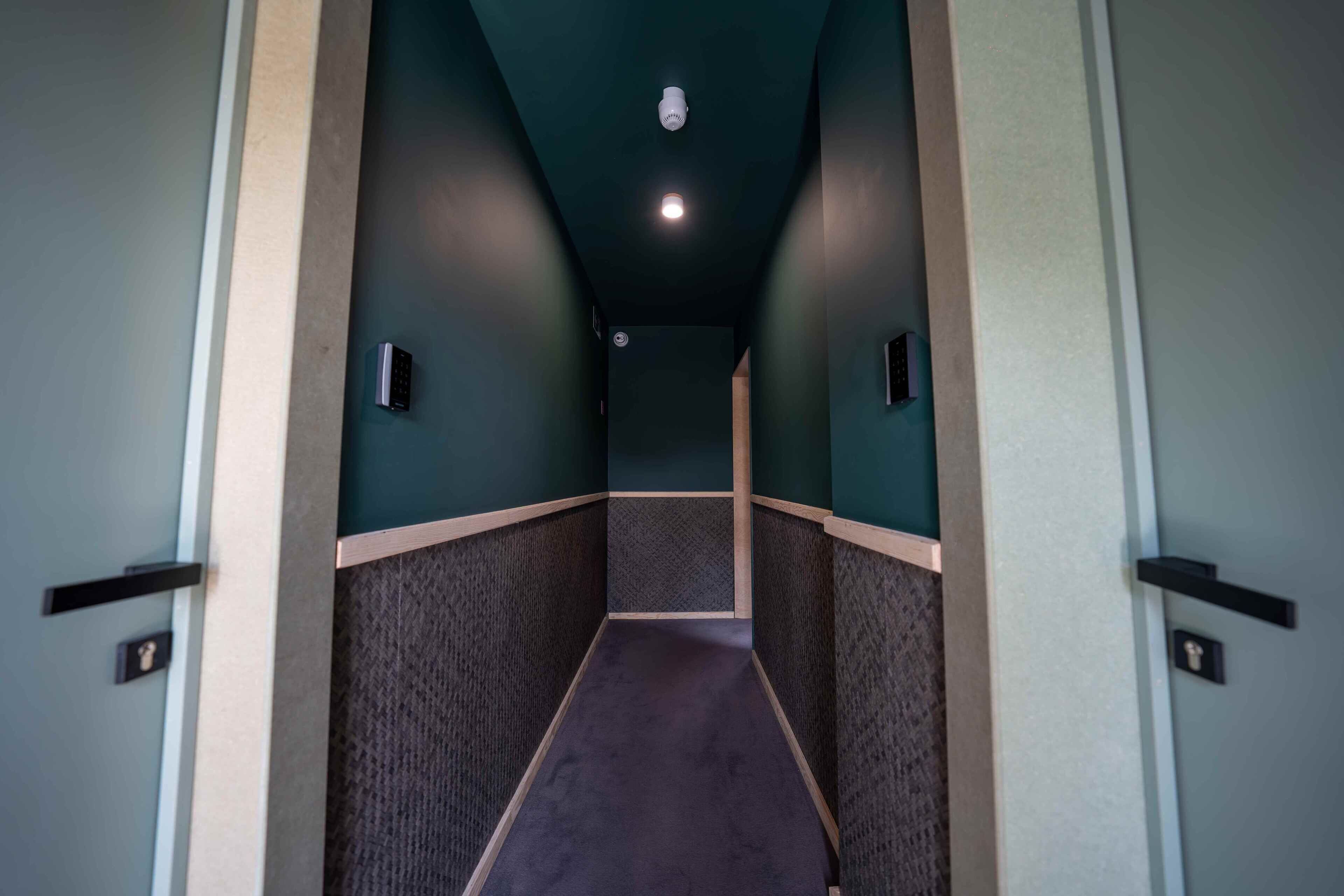 A hallway with a textured floor, dark walls, and a ceiling light.