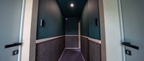 A hallway with a textured floor, dark walls, and a ceiling light.