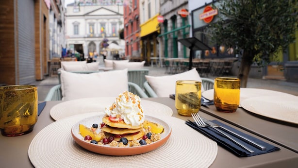 A table set with a dessert, glasses, and cutlery in an outdoor cafe setting.