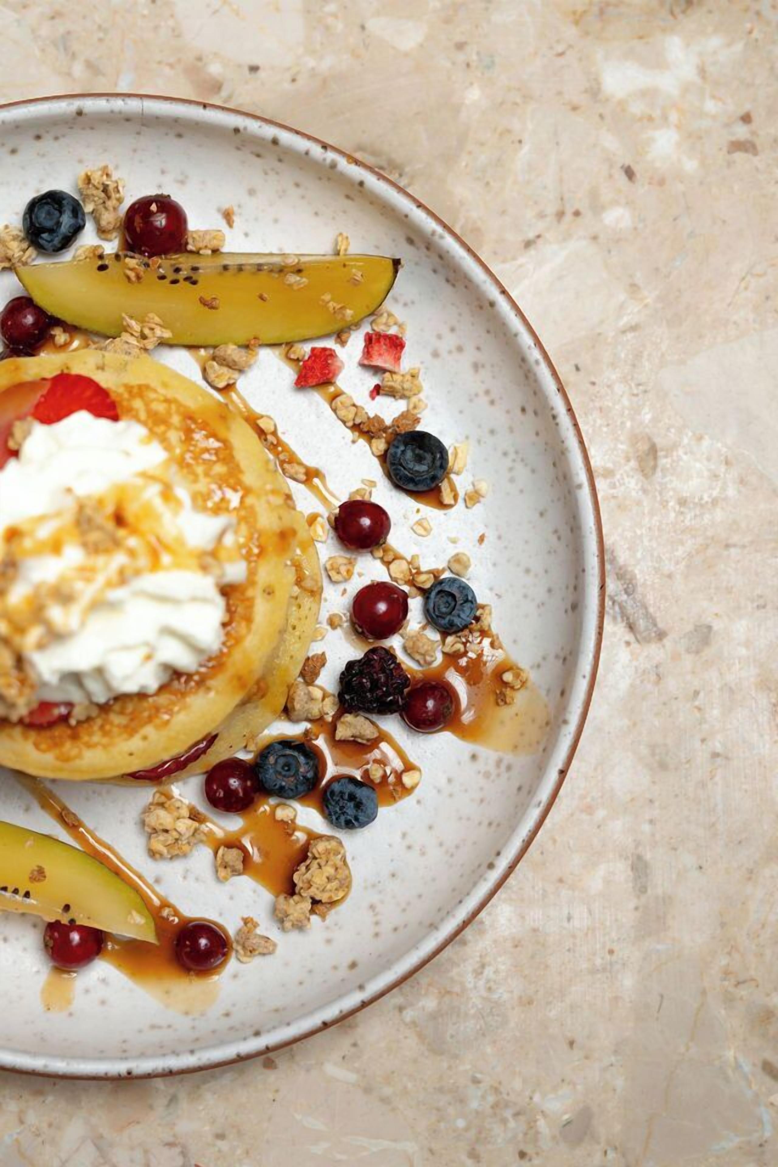 A plate with pancakes topped with whipped cream, blueberries, and a drizzle of syrup.