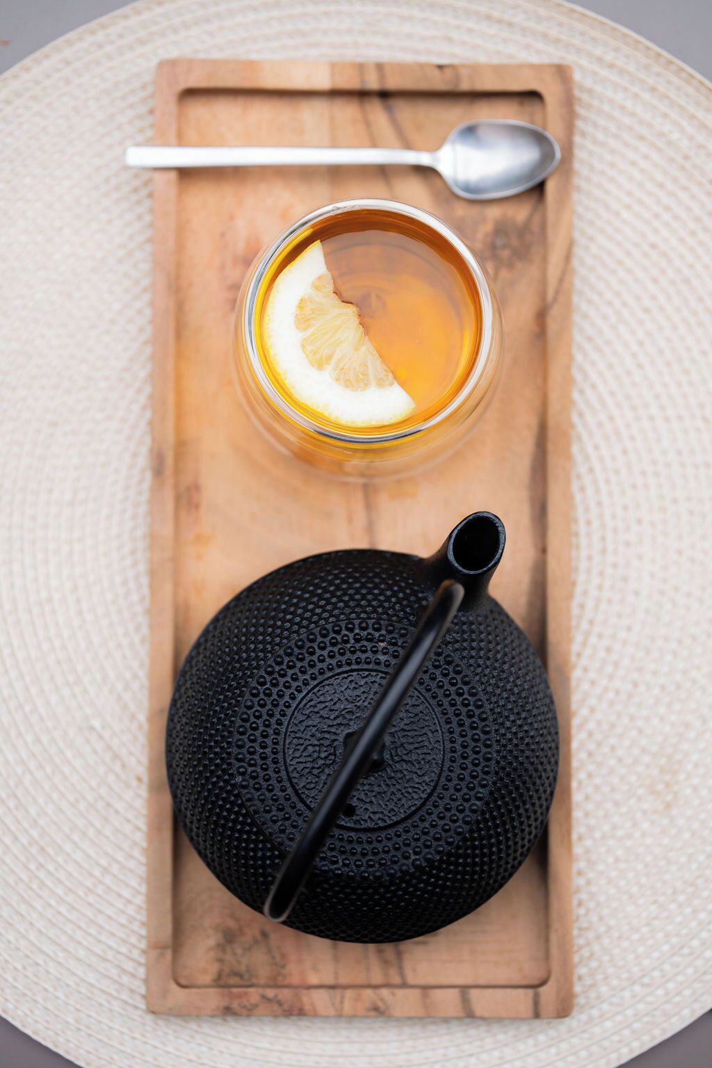 A wooden tray with a glass of tea, a spoon, and a black textured object.